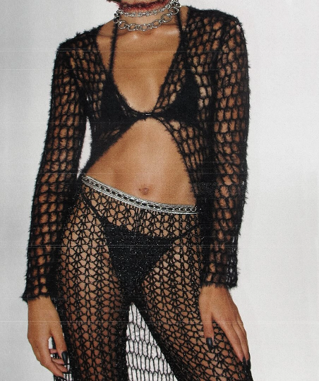 Look feminino preto em tricot vazado com transparência, composto por cardigan de mangas longas felpudo, top biquíni e calça de crochê com cinto prateado de corrente.