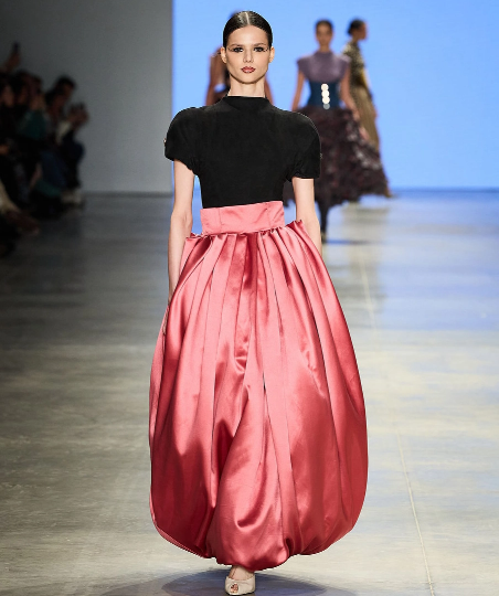 Modelo desfilando na passarela com vestido de saia longa balonê rosa acetinada e blusa preta de gola alta com mangas curtas. Modelo desfilando na passarela com vestido de saia longa balonê rosa acetinada e blusa preta de gola alta com mangas curtas.