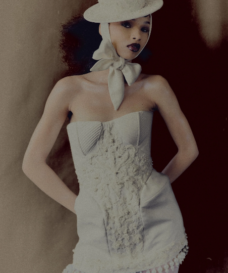 Modelo usando vestido tomara que caia tom off-white com bordados em relevo, chapéu estruturado com laço amarrado no pescoço e detalhes em pérolas na barra.